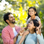 Happy mother with father carrying their daughter on shoulder at park